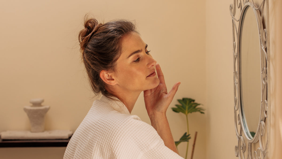 young brunette woman applying skincare in front of mirror