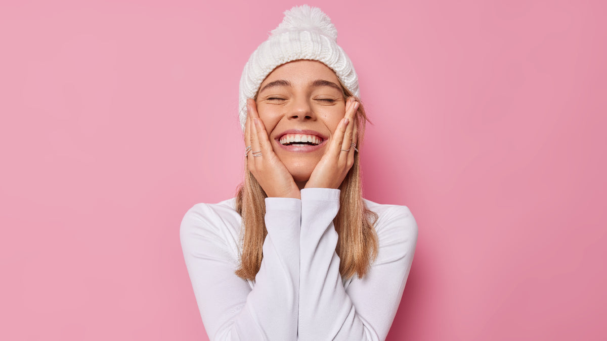 blonde girl in white beanie touching face on pink background
