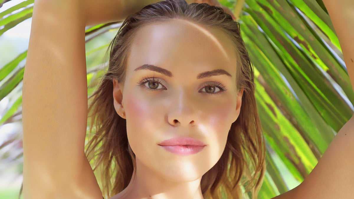 young blonde woman catching shade underneath tropical leaf