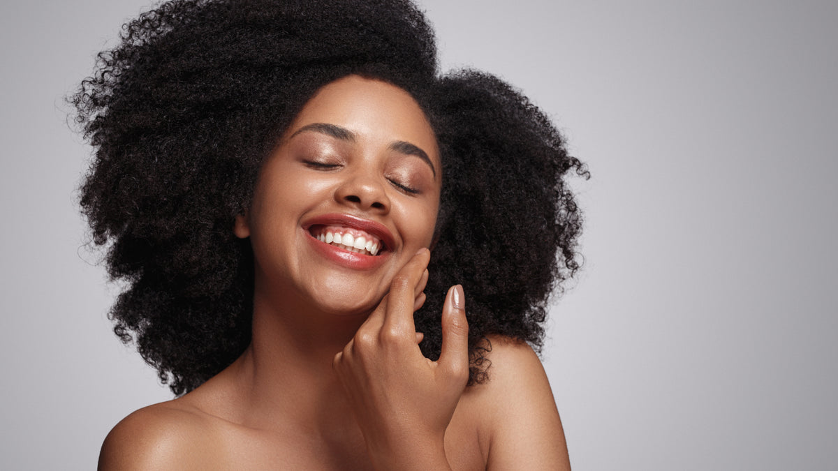 Beautiful black woman with bare skin touching face and smiling