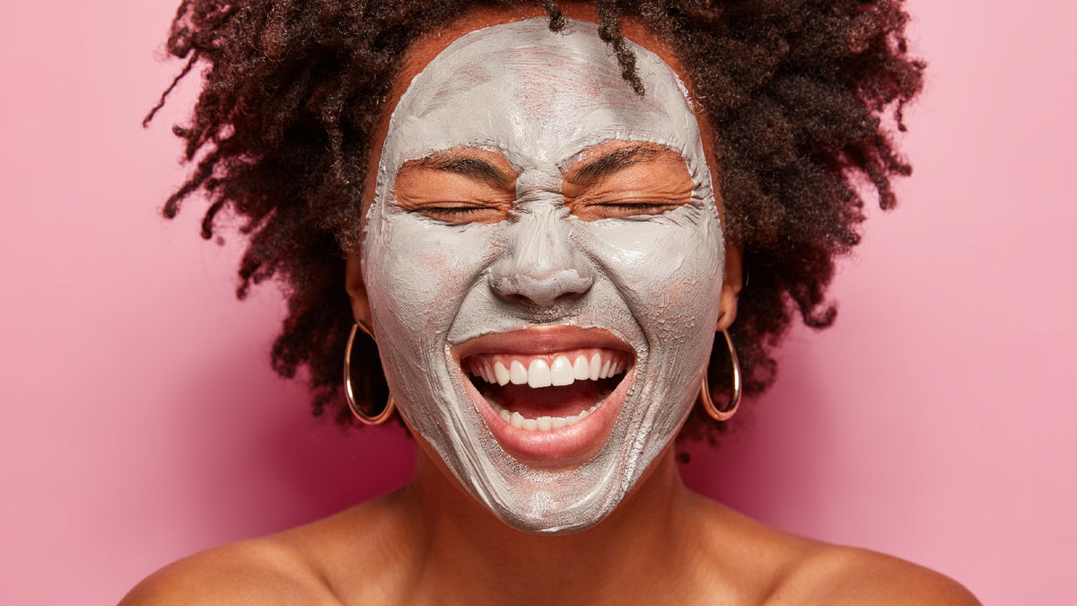 beautiful black girl wearing face pack and laughing on pink background