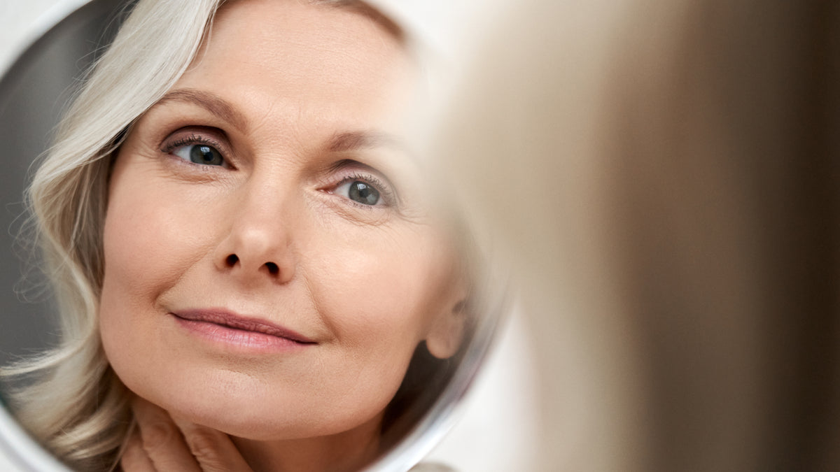 Grey haired woman looking at her great skin in the mirror