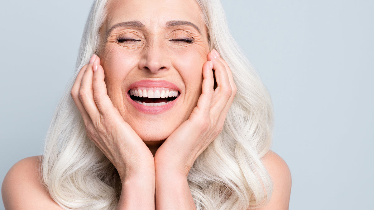 silver haired women laughing and touching face on gray background