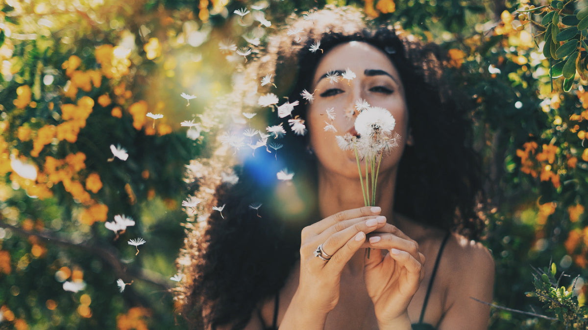 black girl in front of flowers, blowing dandelion