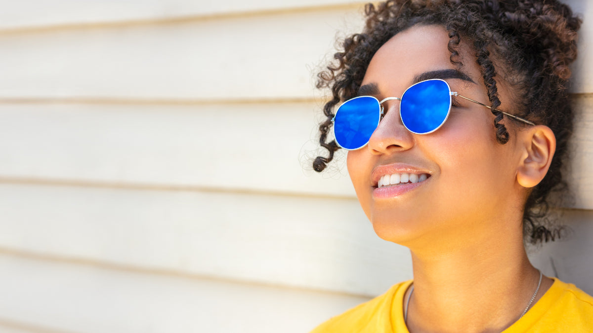 young woman smiling against wall wearing sunglasses