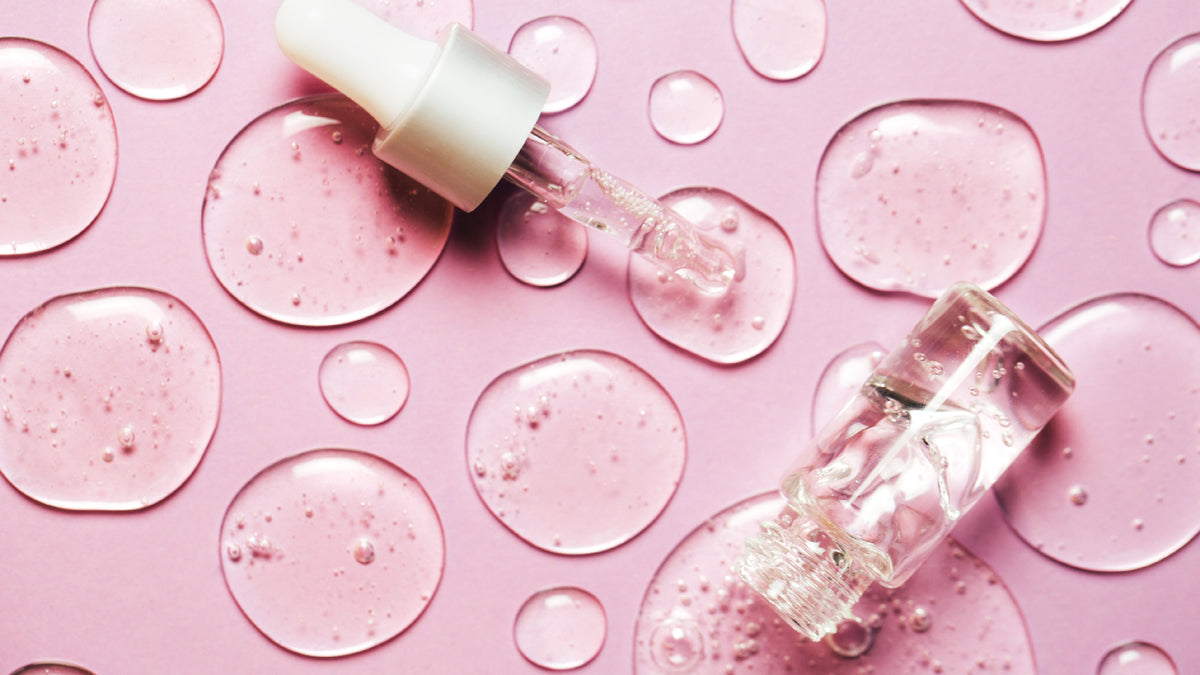 facial serum bottle, dropper and blobs on pink background