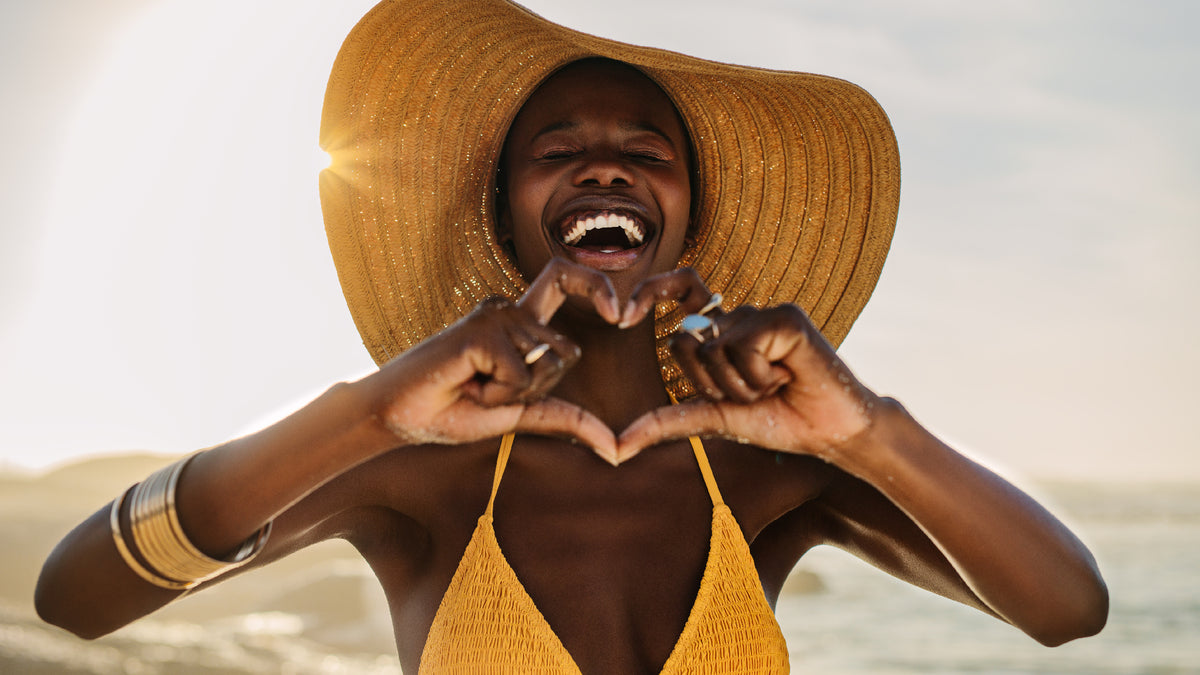 black woman on beach in bikini making heart sign with hands