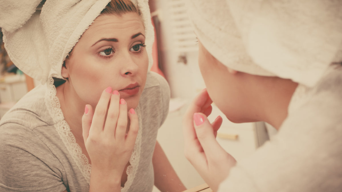 brunette girl studying skin in the mirror with towel on head