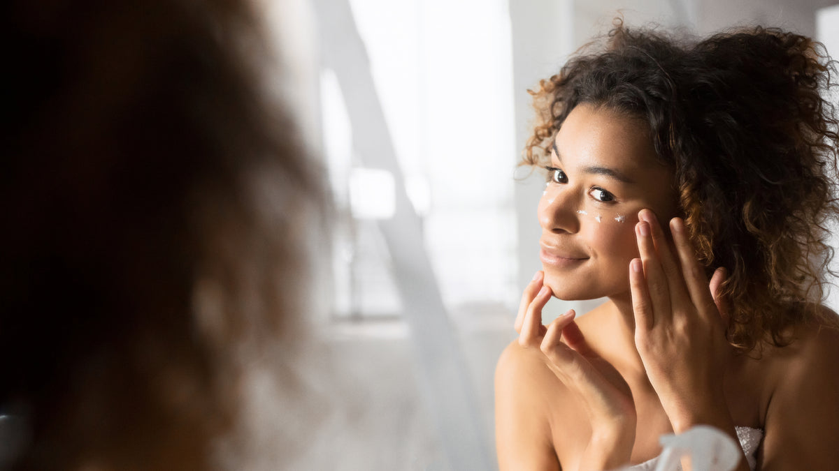 beautiful black woman applying eye cream in mirror
