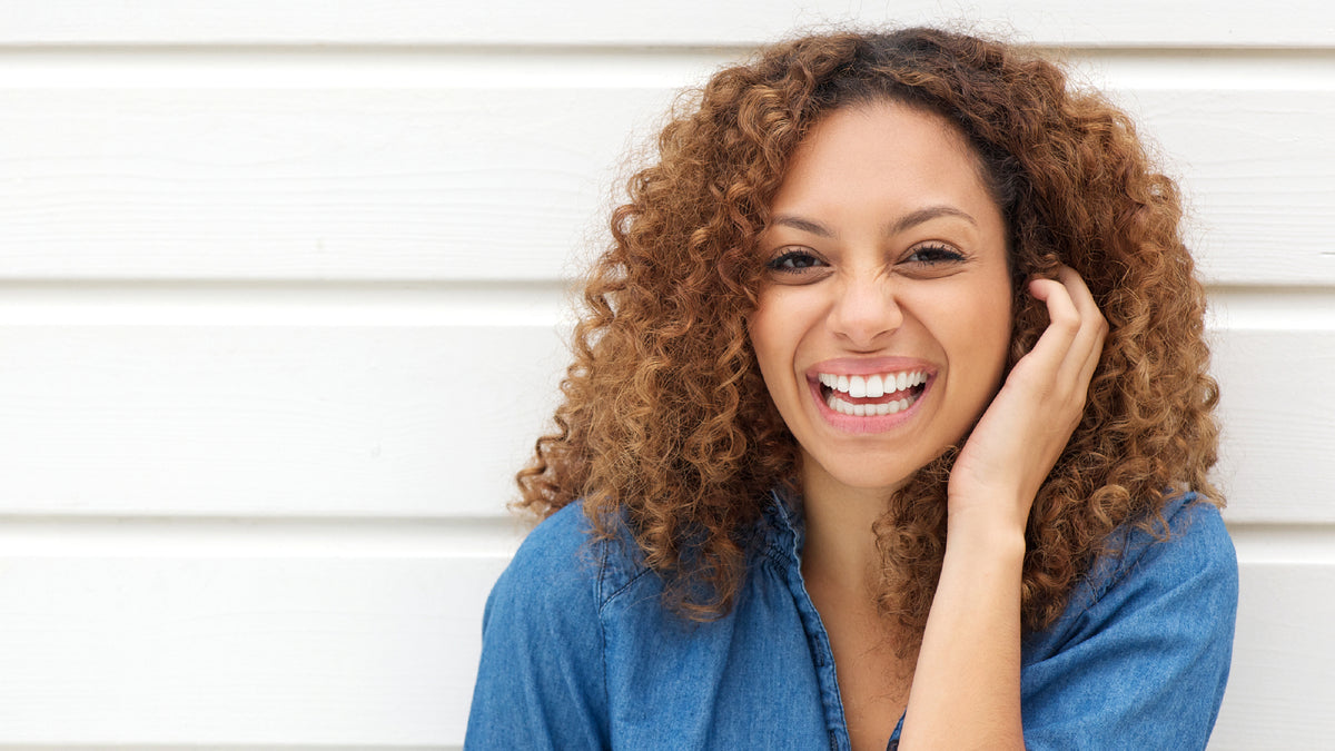 young woman laughing touching face in front of white fence