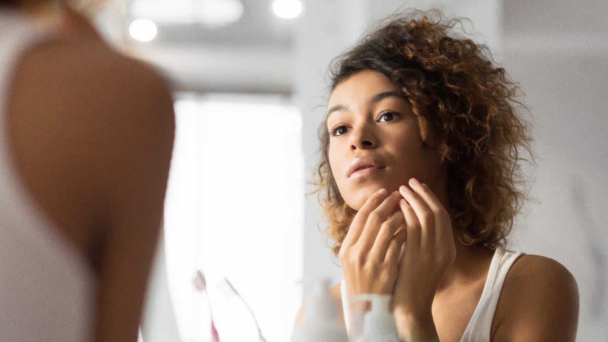 young woman touching skin and squeezing pimple in mirror