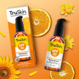 Packaging and bottle of TruSkin SPF 30 Mineral Sunscreen Facial Serum with orange slices, sunflowers, and leaves on an orange background.