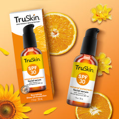 Packaging and bottle of TruSkin SPF 30 Mineral Sunscreen Facial Serum with orange slices, sunflowers, and leaves on an orange background.